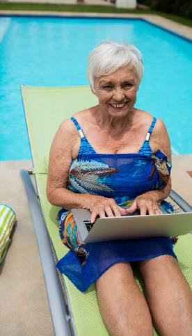 Old woman looking at laptop by pool